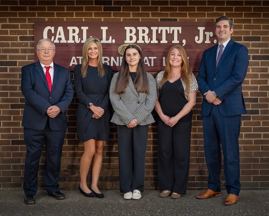 The firm's attorneys and staff standing in front of the CARL L. BRITT, Jr. sign on the brick office wall